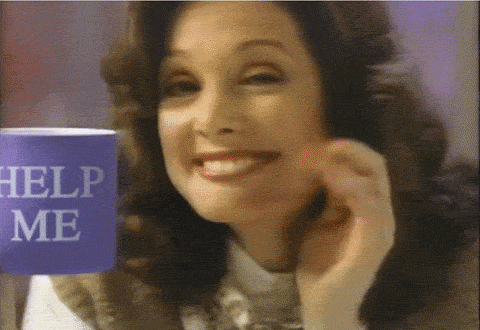 Blurry old footage of a woman with early 90s hair smiles as she holds up a mug that says Help Me.