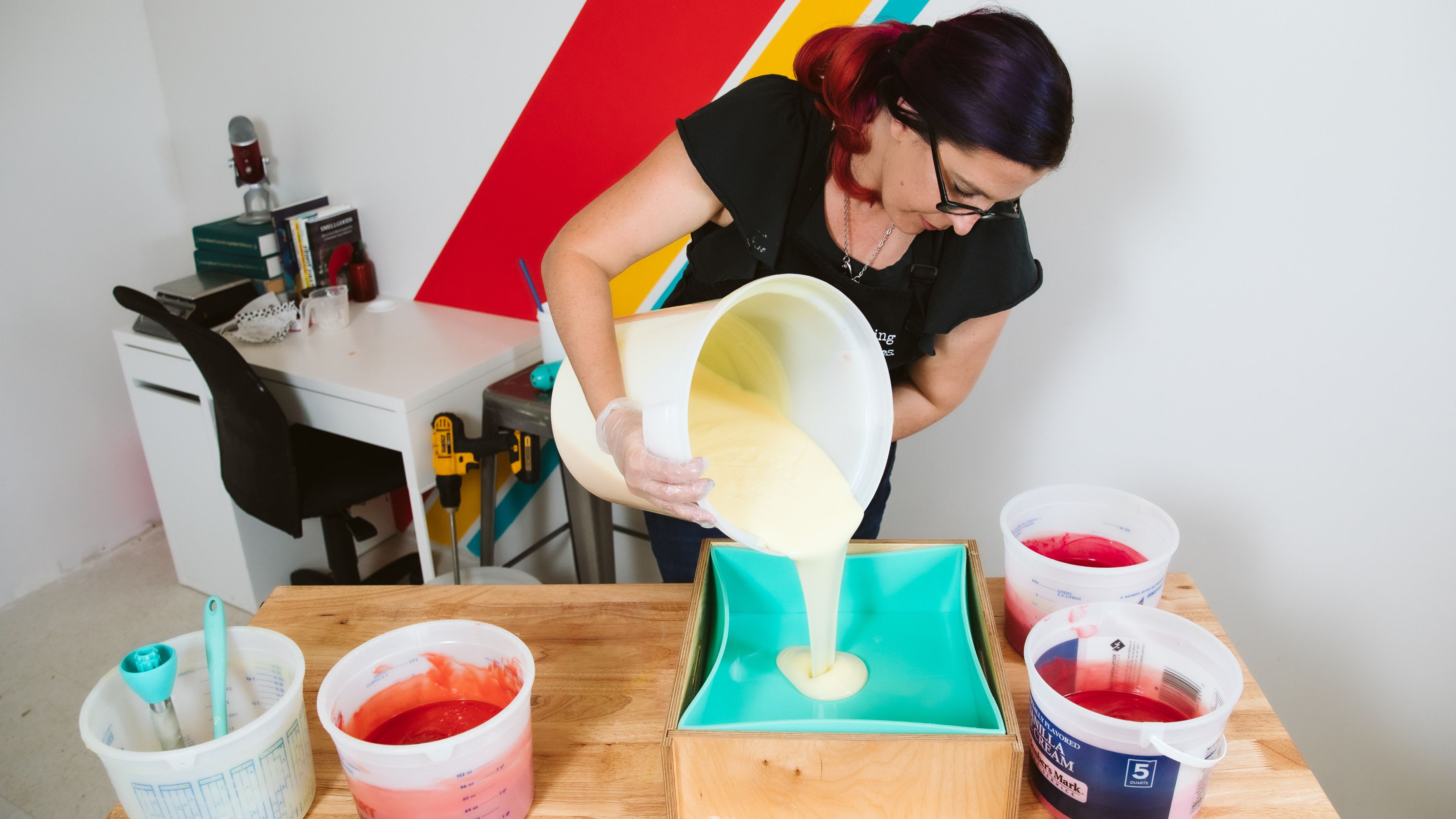 Kenna pours white soap batter into a large rectangular wooden mold.
